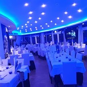 Hochzeitslocation - Unser Hauptsaal, weiße Tischdecke und Servietten, Kerzen, Blaues licht und DJ Station - Ristorante Il Pescatore