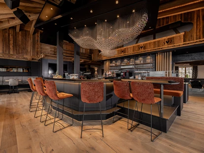 Destination-Wedding - Exklusivität - Wilder Kaiser - Unser Stolz: unsere kommunikative und große Bar, eingebettet in die Kombination von traditionellem Hüttenambiente mit viel Altholz und modernem Style. Sie lädt ein zum Verweilen mit Freunden, zum gemeinsamen Drink während der Partynacht oder einfach zum Genießen der wunderschönen Aussicht. Highlight ist unser Kristall-Adler, welcher für ein besonderes Ambiente sorgt und abends unser Restaurant in ein besonderes Licht verzaubert. - jezz AlmResort Ellmau